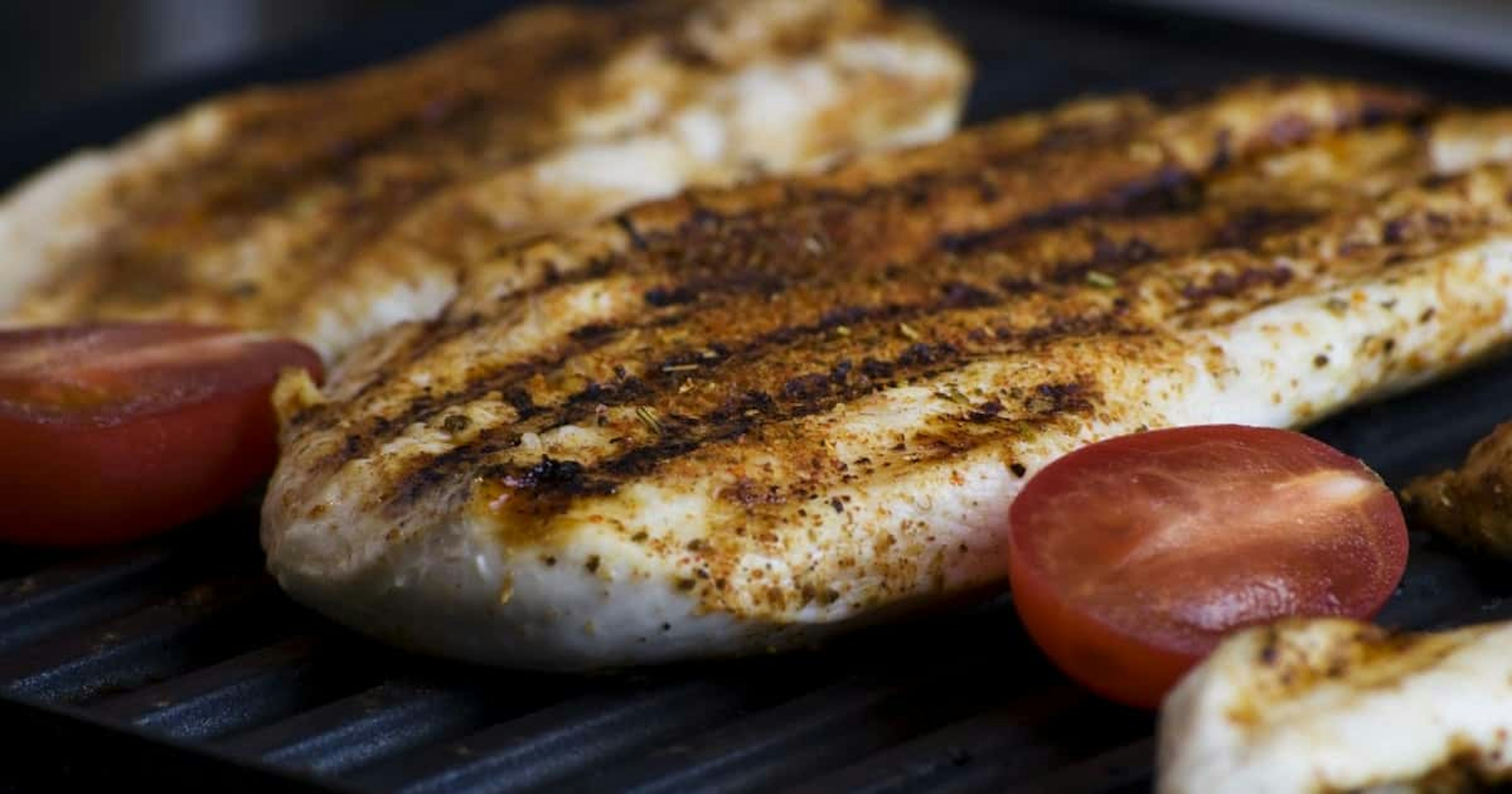 Seasoned chicken breast on a grill with tomatoes